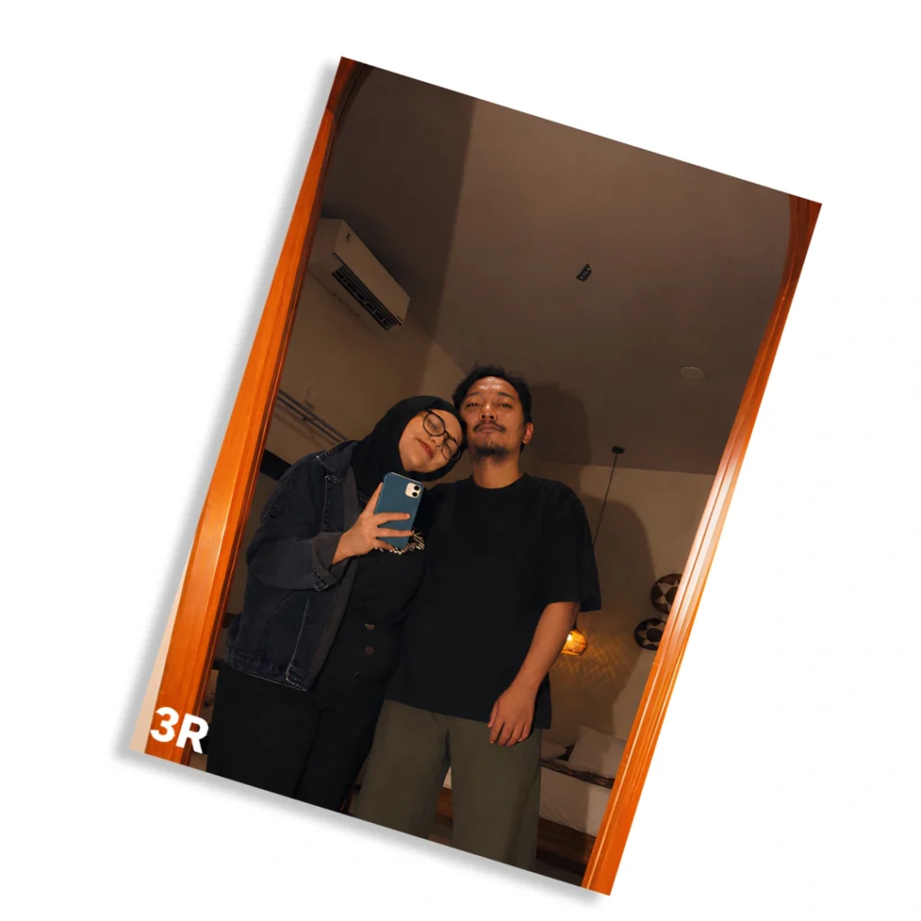 Sepasang pria dan wanita berfoto di depan cermin hasil cetak foto 3R dengan bingkai kayu minimalis.