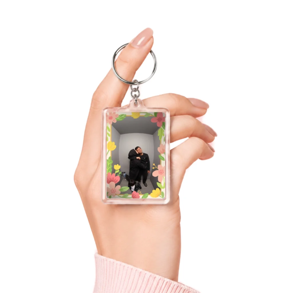 Tangan memegang ganci rectangle 2 muka akrilik transparan dengan foto berbingkai bunga warna-warni yang lucu.