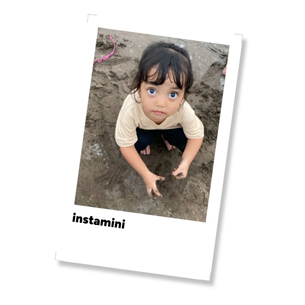 Seorang balita bermain pasir di pantai dalam tampilan polaroid instamini yang manis.