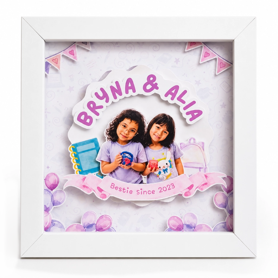 Bingkai 3D putih berisi foto timbul dua anak perempuan dan teks Bryna & Alia sebagai inspirasi kado unik perpisahan.
